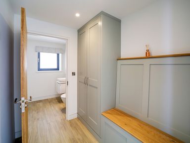 A hallway with built in cabinets and a wooden bench leading to a bathroom with a window at Megizzy in Polzeath