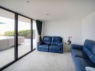 A living room with two blue leather sofas glass side table with plant and sliding glass door at Megizzy in Polzeath