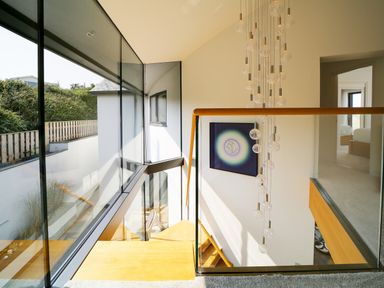 A stairwell with glass railings a hanging light fixture and a painting on the wall at Megizzy in Polzeath