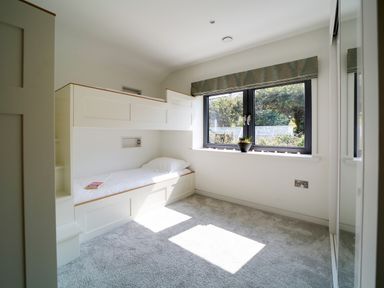 A bedroom with a bunk bed a window with a plant and a carpeted floor at Megizzy in Polzeath