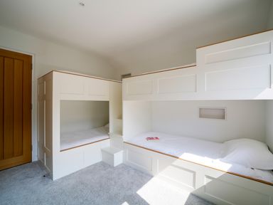 A bedroom with white built-in bunk beds and a wooden door at Megizzy in Polzeath