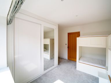 A bedroom with a bunk bed a wooden door and a mirrored sliding closet door at Megizzy in Polzeath