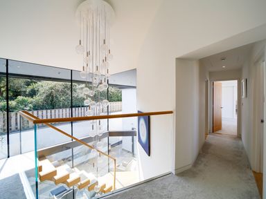 A hallway with carpet next to a staircase with glass railing and hanging light at Megizzy in Polzeath