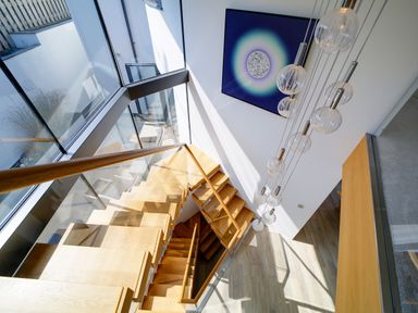 A wooden staircase with glass railing and hanging round light fixtures at Megizzy in Polzeath