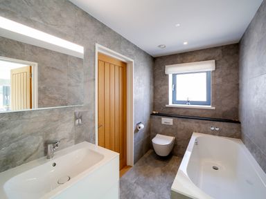 A bathroom with a sink, wooden door, toilet, bathtub, and a window at Megizzy in Polzeath