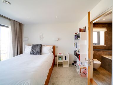 A bedroom with a bed white bedding a bookshelf and an open door to a bathroom at Megizzy in Polzeath