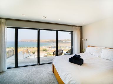 A bedroom with a bed and folded towels facing glass sliding doors overlooking a coastal view at Megizzy in Polzeath