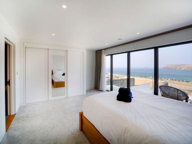 A bedroom with a bed and large windows overlooking the sea at Megizzy in Polzeath