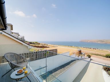 A balcony with a wicker chair and table with croissants and juice overlooking the sea at Megizzy in Polzeath