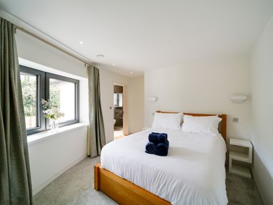 A bedroom with a wooden bed with white linens and three blue towels on it two white bedside tables a window with closed green curtains and a vase with flowers on the sill at Megizzy in Polzeath