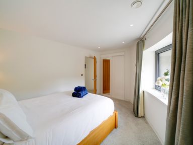 A bedroom with a wooden bed white bedding blue towels a window with curtains and a vase of flowers at Megizzy in Polzeath
