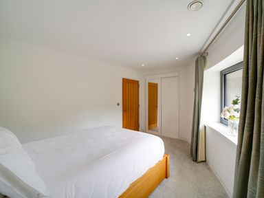 A bedroom with a wooden bed a window with curtains and a vase of flowers at Megizzy in Polzeath
