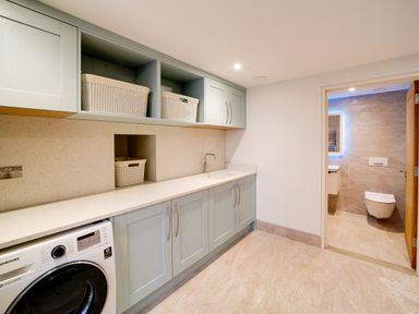 A laundry room with cabinets washing machine and baskets next to a bathroom at Megizzy in Polzeath