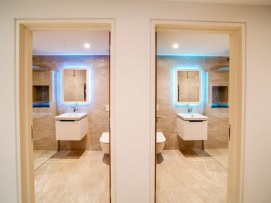 Two identical bathrooms each with a floating white sink, illuminated rectangular mirror, tiled walls and floors at Megizzy in Polzeath