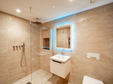 A bathroom with a walk-in shower a wall-mounted sink and an illuminated mirror at Megizzy Polzeath