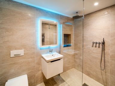 A bathroom with a wall-mounted sink under a backlit mirror next to a walk-in shower at Megizzy in Polzeath