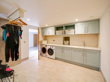 A laundry room with washing machine and dryer under built-in cabinets and wetsuits hanging at Megizzy in Polzeath