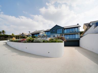 A modern house with large glass windows and a landscaped garden with plants in front at Megizzy in Polzeath