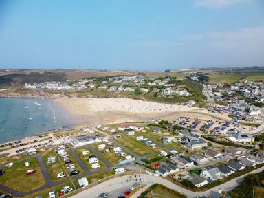 A coastal town with a sandy beach parking lots RVs and houses near the shore at Megizzy in Polzeath