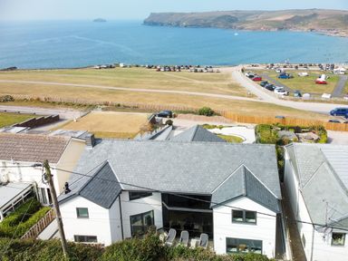 A coastal view with modern houses near a parking area and a grassy field by the sea at Megizzy in Polzeath