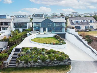 Modern house with lawn driveway and garden in front surrounded by neighboring houses at Megizzy in Polzeath