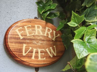 A wooden sign with the words Ferry View surrounded by green leaves