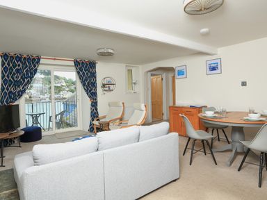 A living room with a sofa two armchairs a round dining table with chairs and a balcony with water view at Ferry View Dartmouth