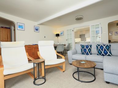 A living room with two white chairs a gray sofa with patterned cushions a round wooden coffee table and a dining table with gray chairs at Ferry View in Dartmouth