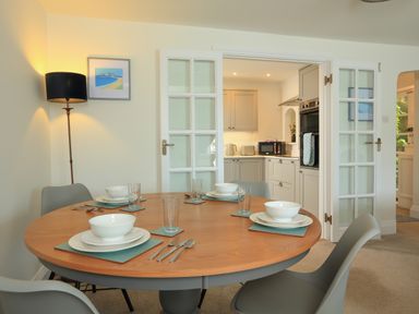 A dining area with a round wooden table set with bowls plates glasses and cutlery and grey chairs near glass doors leading to a kitchen at Ferry View in Dartmouth