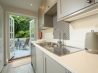 A kitchen with a sink and cabinets looking out to an outdoor patio with a table and chairs at Ferry View in Dartmouth
