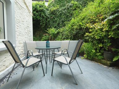A small outdoor patio area with four chairs around a round glass table surrounded by green plants at Ferry View in Dartmouth