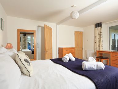 A bedroom with a bed with white linens and a navy throw with towels on it a wooden dresser a desk with a chair and a mirror at Ferry View in Dartmouth