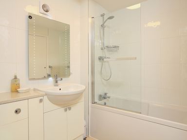 A bathroom with a sink and mirror next to a bathtub with a shower screen at Ferry View in Dartmouth