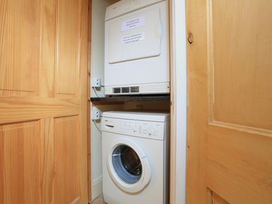 A stacked white washing machine and dryer in a small wooden closet at Ferry View in Dartmouth