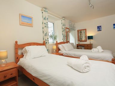 A bedroom with two single beds wooden furniture and rolled towels at Ferry View in Dartmouth