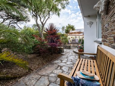 An outdoor patio with a wooden bench stone pathway garden plants and a table with chairs under an umbrella at Longhouse Bungalow in Rock
