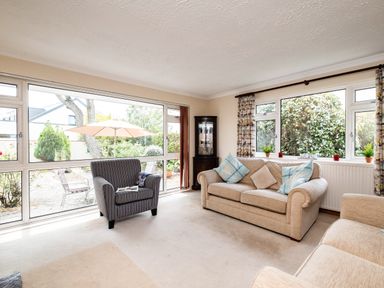 A sitting room with beige sofas blue cushions and a striped armchair near large windows at Longhouse Bungalow in Rock