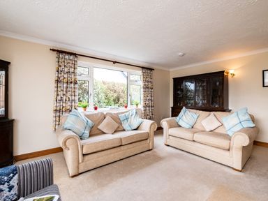 A living room with two beige sofas with cushions a dark wood cabinet and a window with patterned curtains at Longhouse Bungalow in Rock