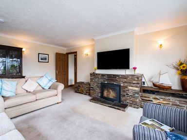 A living room with a beige sofa and pillows a stone fireplace with a mounted TV and decorative sailboat at Longhouse Bungalow in Rock