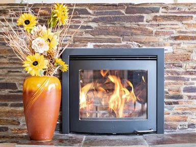 A fireplace with a burning fire and a vase with yellow flowers on a stone wall at Longhouse Bungalow in Rock