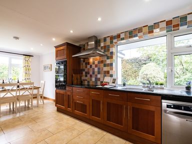 A kitchen with wooden cabinets and tiled backsplash next to a dining area with a wooden table and chairs at Longhouse Bungalow in Rock