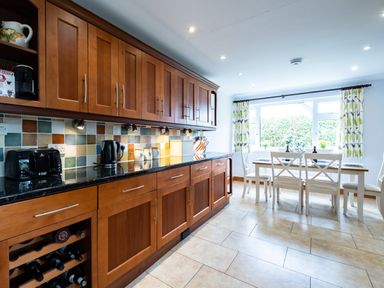 A kitchen with wooden cabinets and a dining table with white chairs by a large window at Longhouse Bungalow in Rock