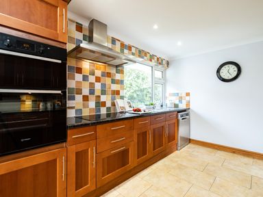 A kitchen with wooden cabinets and multicolored tiled backsplash with a wall clock at Longhouse Bungalow in Rock