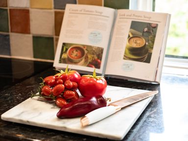 A kitchen countertop with tomatoes a red pepper a knife and an open cookbook featuring soup recipes at Longhouse Bungalow in Rock