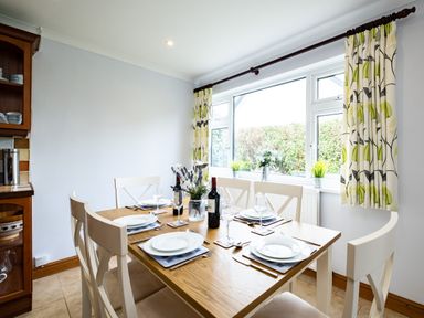 A dining room with a wooden table set for six and floral curtains by a window at Longhouse Bungalow in Rock