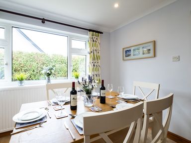 A dining table set with plates wine glasses and bottles in a room with windows and framed pictures at Longhouse Bungalow in Rock
