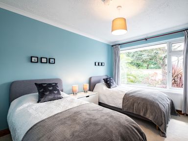 A bedroom with two single beds nightstand with lamps and a large window showing garden at Longhouse Bungalow Rock