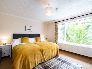 A bedroom with a double bed two bedside tables lamps a window with curtains and a framed picture on the wall at Longhouse Bungalow in Rock
