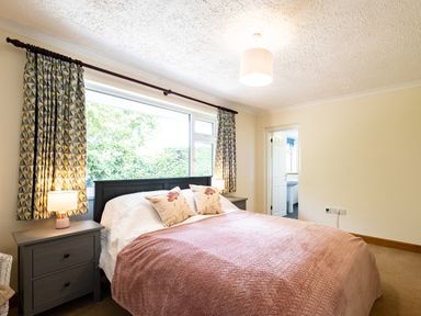 A bedroom with a bed covered in a pink blanket and two pillows bedside tables with lamps and a window with curtains at Longhouse Bungalow in Rock