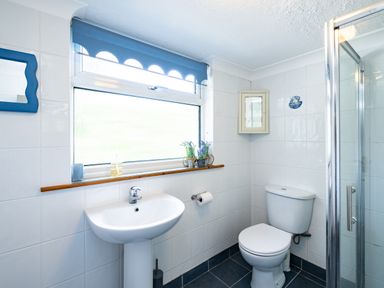 A bathroom with a sink toilet shower mirror and window with blue blind at Longhouse Bungalow in Rock